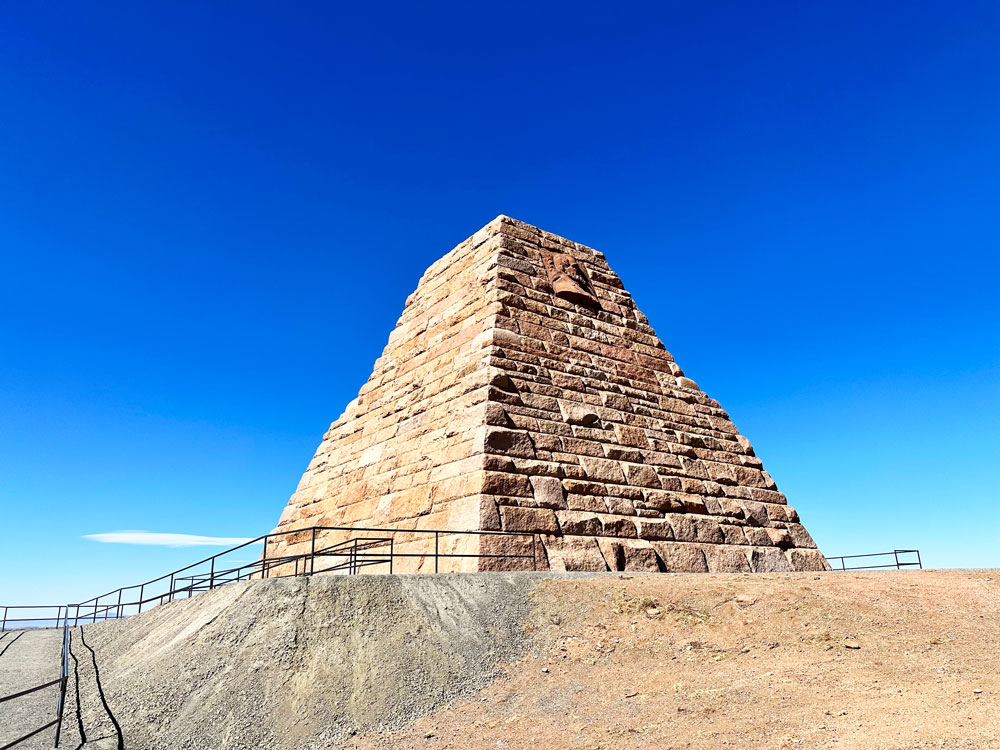 The Ames Monument, a large pyramid-shaped structure made of stone, under the vast blue Wyoming sky.