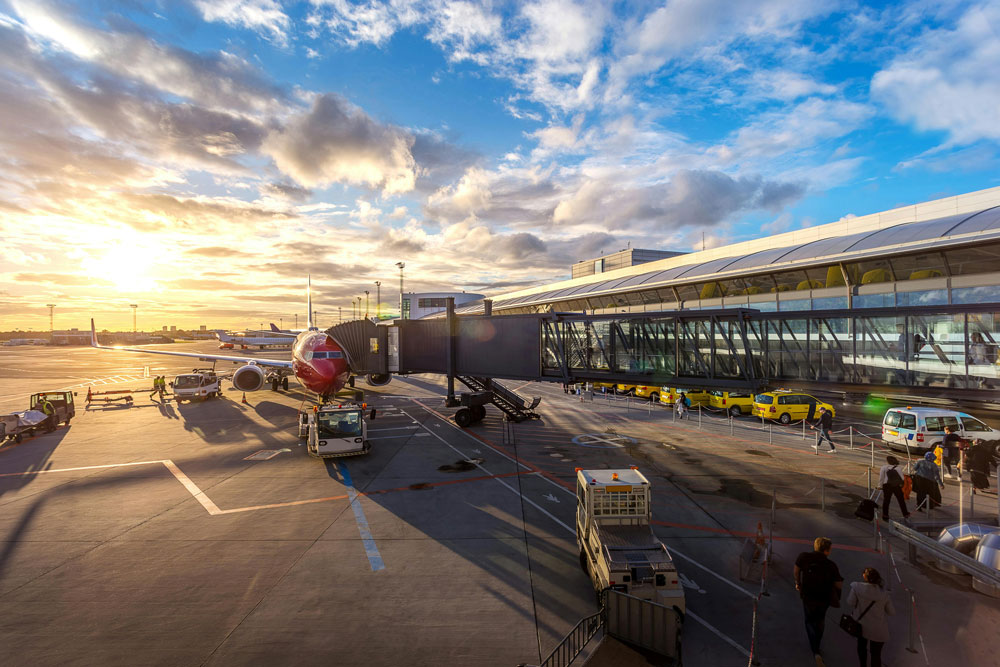 A busy airport scene with passengers, ground crew, and an aircraft at the gate during a vibrant sunset