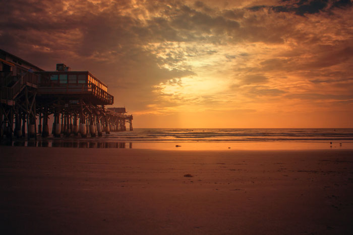 Warm sunset hues cast over a peaceful beach setting with a wooden pier in the background, capturing the tranquil atmosphere of Cocoa Beach