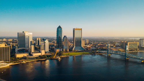 Golden hour over Jacksonville skyline with the sun reflecting off the river and high-rise buildings, showcasing the city's modern architecture.