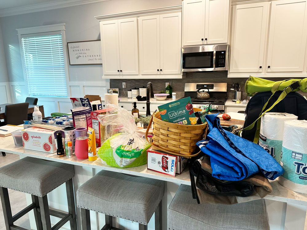 A kitchen island cluttered with groceries an items for a camping trip including, sunscreen, bug spray, paper towels, and a basket among other things