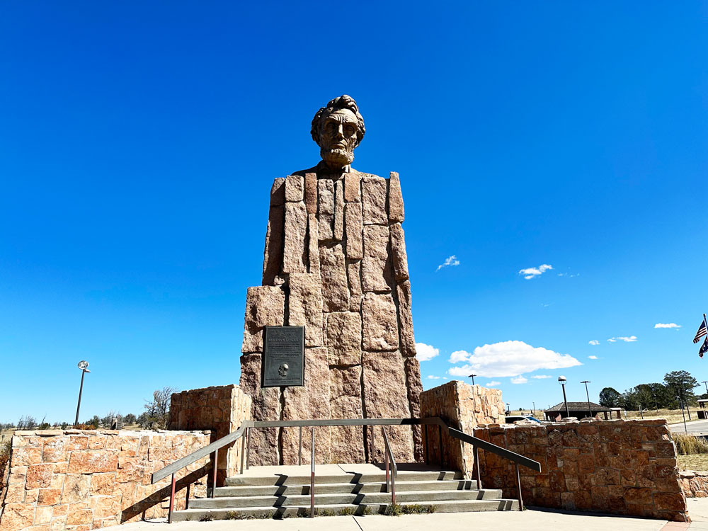 Tall statue of Abraham Lincoln built with a mosaic of stone blocks, standing prominently against a blue sky in Wyoming