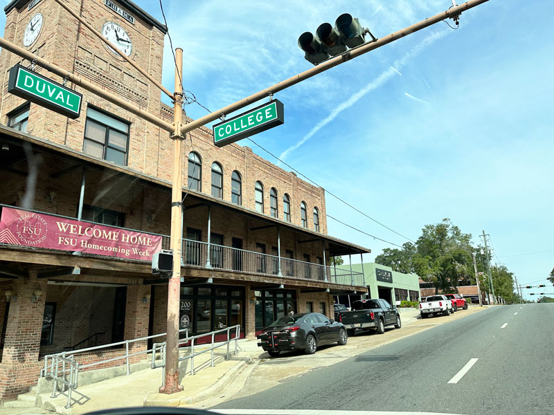 Historic brick buildings at the corner of Duval and College Street in Tallahassee with a 'Welcome Home' banner for FSU Homecoming Week.