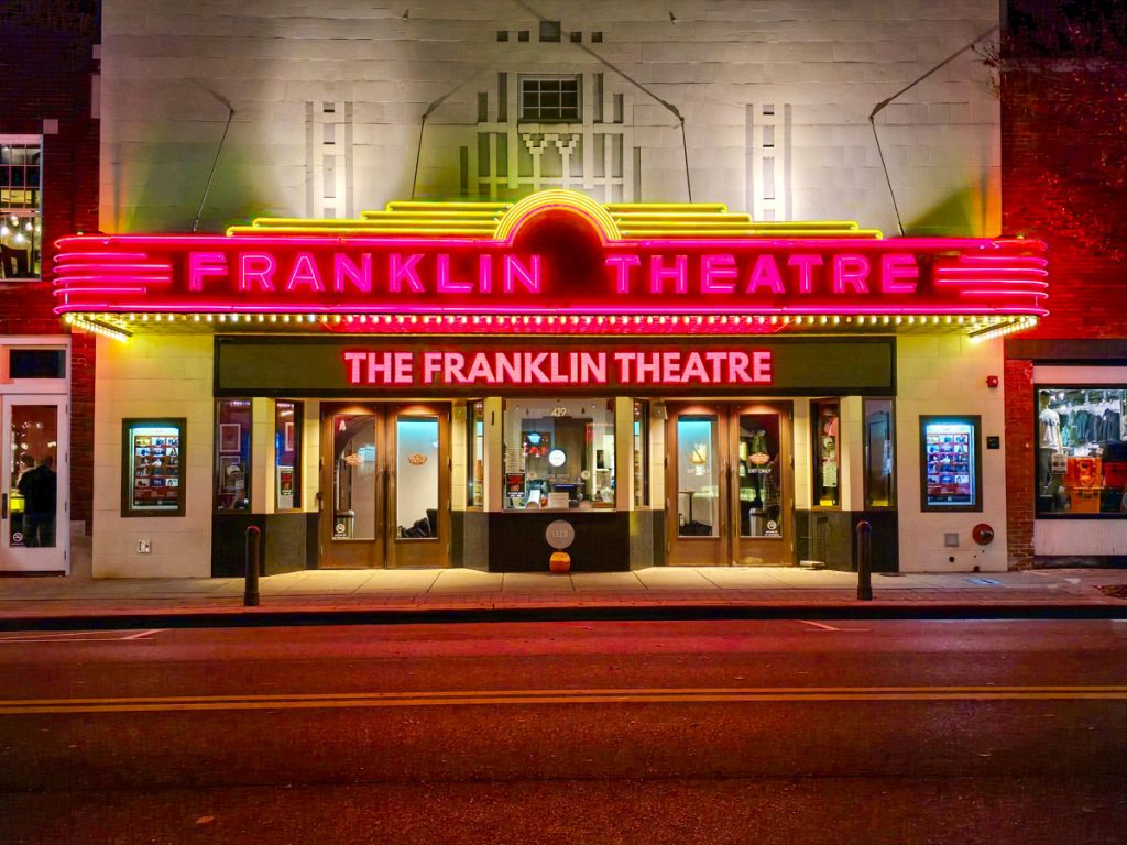 The illuminated facade of the Franklin Theatre at night, glowing with red and yellow neon lights on a quiet street.